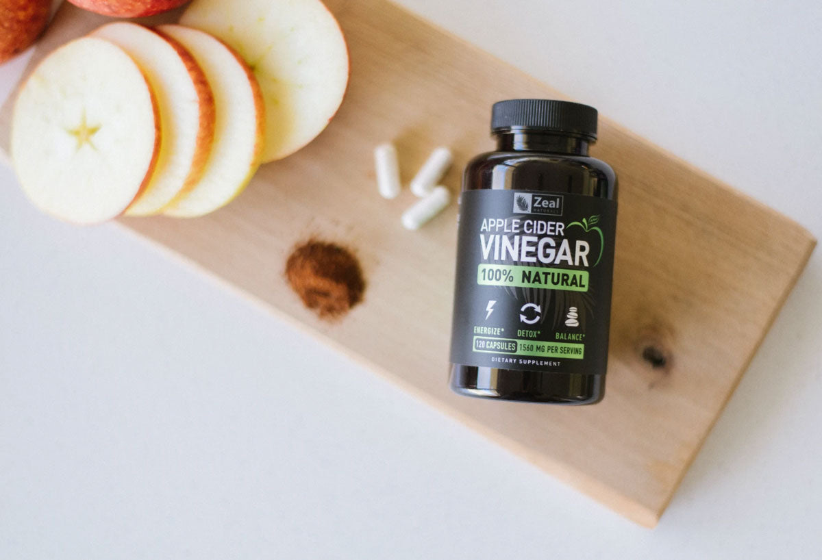 Apple Cider Vinegar capsules on top of a cutting board next to sliced apples, some acv capsules and pepper.